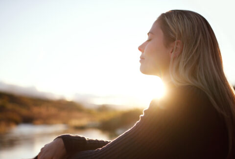 serene woman looking out over denver lake with flare from sun behind her