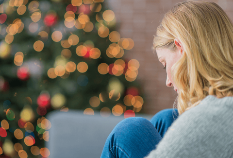 Woman depressed over holidays on couch with lit wreath in background
