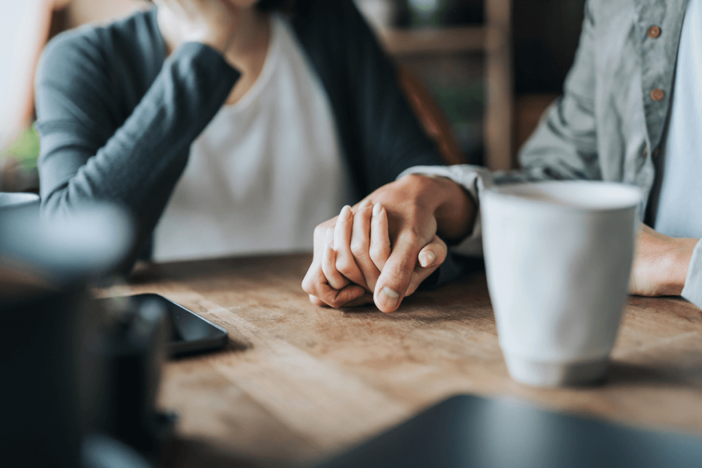 close up couple holding hands and drinking coffee, demonstrating their closeness after getting couples counseling