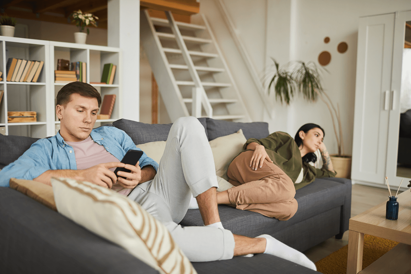 couple sitting apart on couch, he's on phone while she watches tv, indicating they need couples therapy