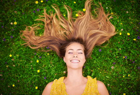 Women with long hair lying on bright green grass, communicating spring happiness after having detox treatment at Ballen Medical & Wellness